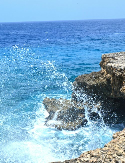 Vibrant ocean waves splashing against the rocky shoreline of Curaçao. A perfect tropical seascape for travel inspiration.